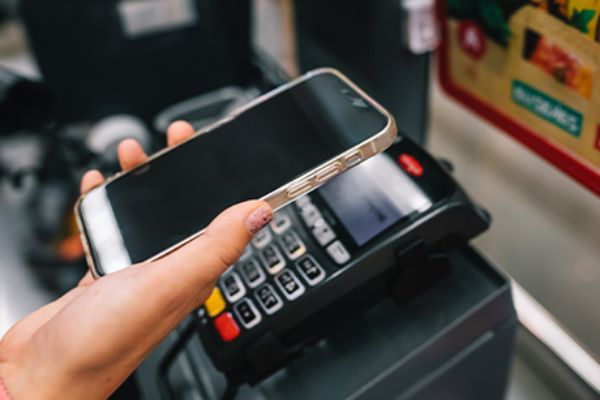 Mit iPhone via Apple Wallet vor einem POS-Bezahlterminal