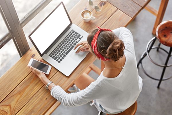 Junge Frau sitzt mit Handy und Laptop in einem Café