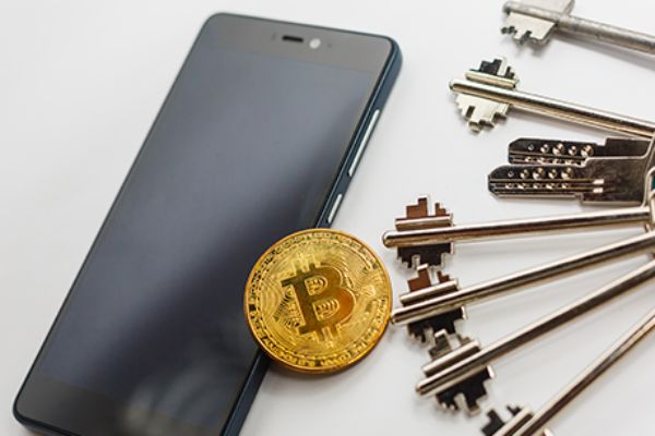 Bitcoin Münze liegt zwischen Smartphone und Schlüsselbund