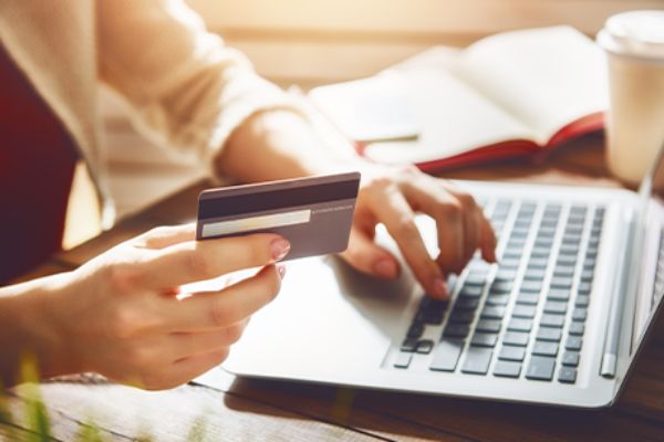 Rechte Hand hält Bankkarte, linke Hand auf Laptop-Tastatur