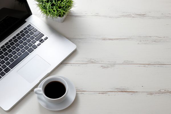 Laptop vor Kaffeetasse auf weißem Tisch 