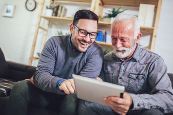 Zwei Männer sitzen vor einem Tablet und amüsieren sich 