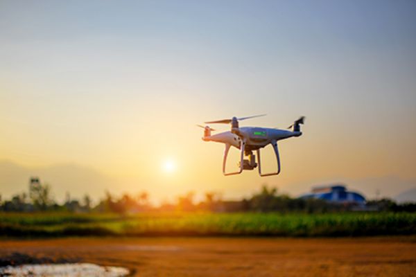 Drohne fliegt über einem Feld vor einem Sonnenuntergang