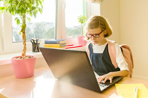 Mädchen mit Schulrucksack sitzt vor einem Laptop.