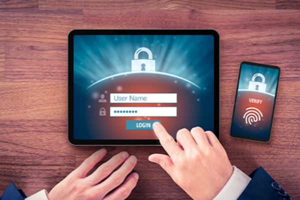 Hände vor einem am Tisch liegenden Tablet und Smartphone mit Fingerabdruck-Biometrie