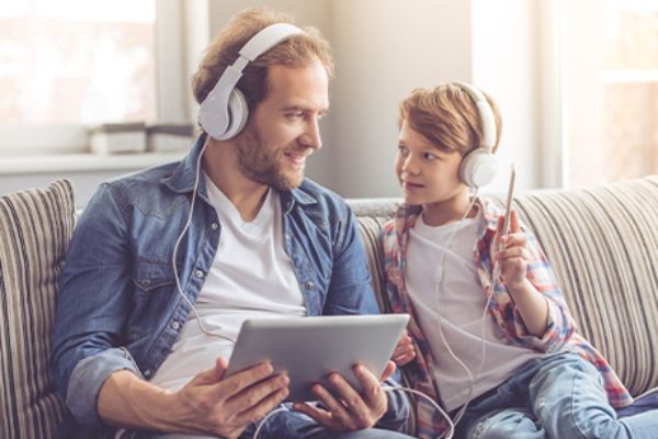 Vater erklärt seinem Sohn sein erstes Handy (auf Couch sitzend)