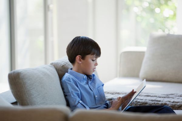 Junge vor einem Tablet sitzt auf einem Sofa 