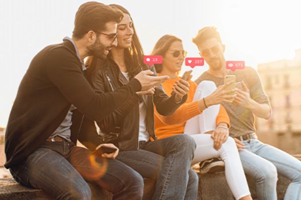 Zwei Männer und zwei Frauen sitzen auf einer Mauer mit Smartphones in den Händen. 
