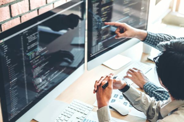 Zwei Personen sitzen vor Monitoren mit Programmcodes