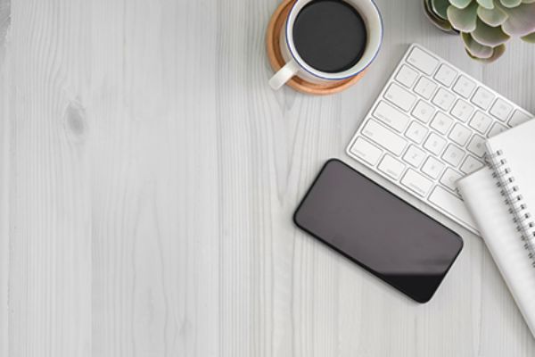Vogelperspektive auf Tastatur, Smartphone, Kaffeetasse und Schreibzeug