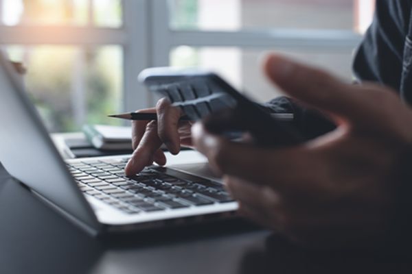 Linke Hand mit Smartphone rechte Hand auf Laptop-Tastatur 