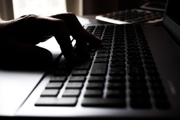 Hand tippt im Dunklen auf Laptop-Tastatur