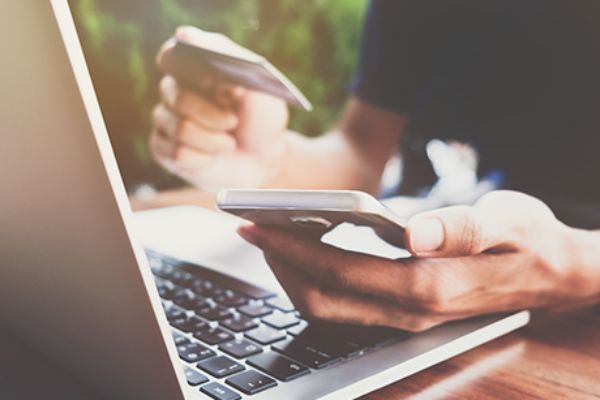 aufgeklappter Laptop und Smartphone, das in einer Hand gehalten wird und in der anderen eine Bankomatkarte