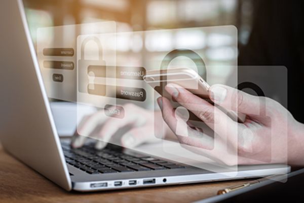 am Laptop werden Passwörter eingegeben und ein Handy wird in der Hand gehalten