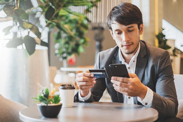 Mann sitzt am Tisch mit Smartphone und Bankkarte in der Hand