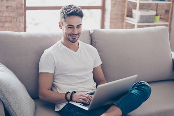 Mann spielt auf der Couch sitzend am Laptop