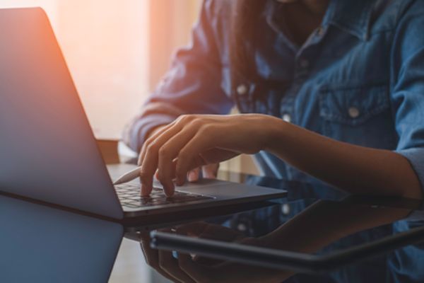 Männlicher Torso sitzt vor offenem Laptop.