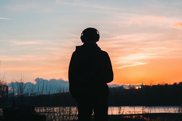 ein einsamer Mann schaut in einen farbenfrohen Sonnenuntergang und hört Musik