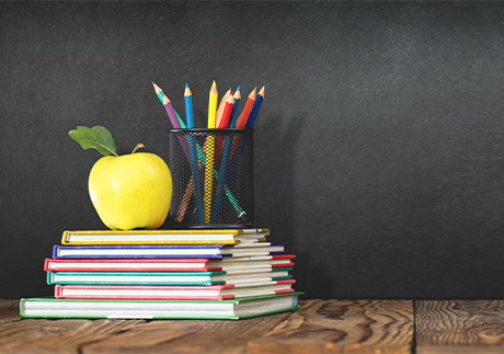 Gestapelte Schulbücher mit Stiften und Apfel darauf 