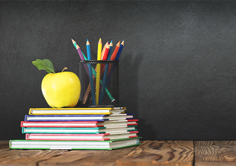 Gestapelte Schulbücher mit Stiften und Apfel darauf