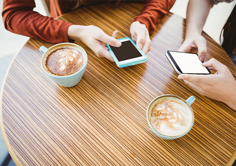 AirDrop: Ausschnitt Hände halten Smartphones vor zwei Kaffeetassen