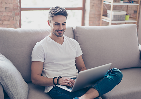 Mann spielt auf der Couch sitzend am Laptop