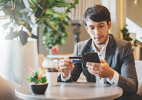 Mann sitzt in einem Cafè und shoppt online via Smartphone