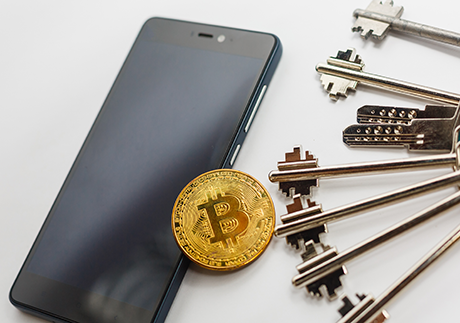 Bitcoin Münze liegt zwischen Smartphone und Schlüsselbund