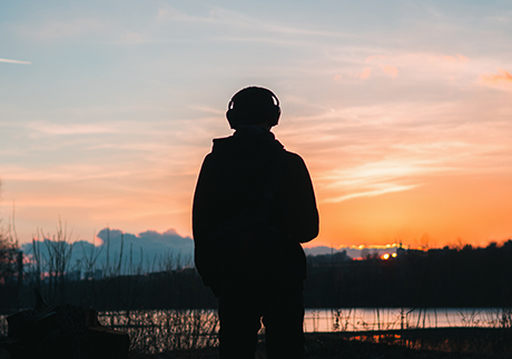 ein einsamer Mann schaut in einen farbenfrohen Sonnenuntergang und hört Musik