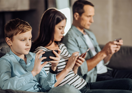 Kind, Frau und Mann sitzen neben einander auf einem Sofa und bedienen Smartphones