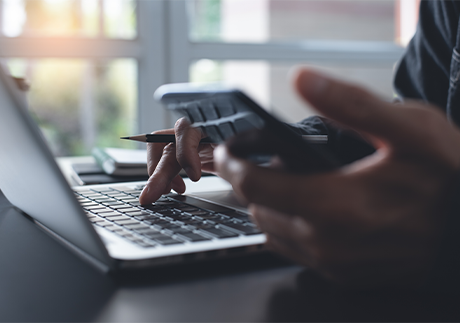 Linke Hand mit Smarphone, rechte Hand auf Laptop-Tastatur.