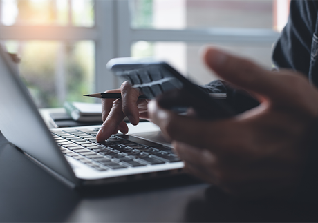 Linke Hand mit Smarphone, rechte Hand auf Laptop-Tastatur. 