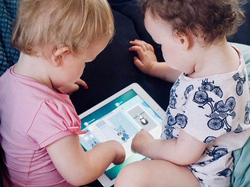 Bild zeigt zwei Babys, die mit einem Tablet spielen.