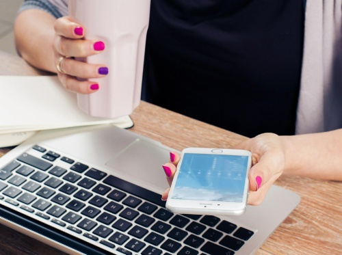 Bild zeigt Person, die Smartphone in der Hand hält und parallel einen Laptop nutzt.