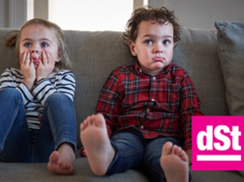 Bild zeigt zwei Kleinkinder, die auf der Couch sitzen.